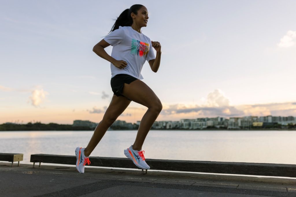 A woman in white t-shirt and black shorts is running with skyline in background. Measure running progress, how to tell if your making progress running, progress in running