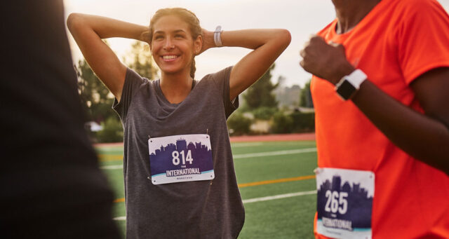 Woman standing on an outdoor track with her hands behind her head wearing a race bib. 5K race tips, how to get 5K ready, 5K running,